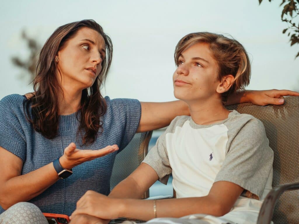 A mother has a conversation with her teenage son. She looks at him and has one hand extended palm up. The boy looks off into the distance.