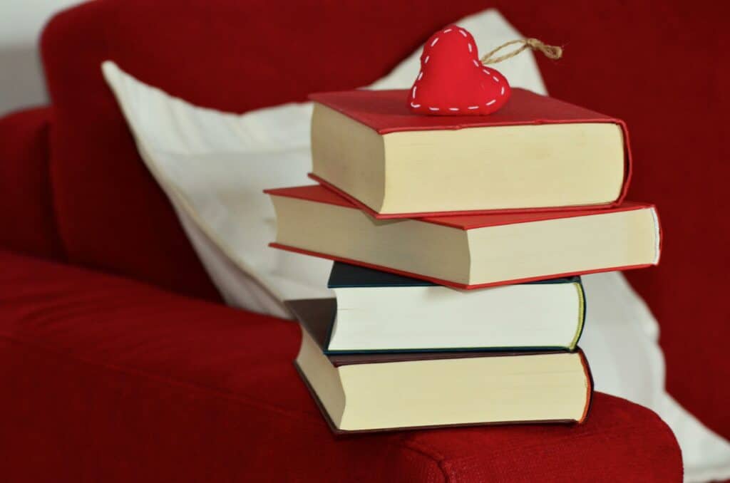 Close-up photo of a stack of four books with a red felt heart ornament on top.