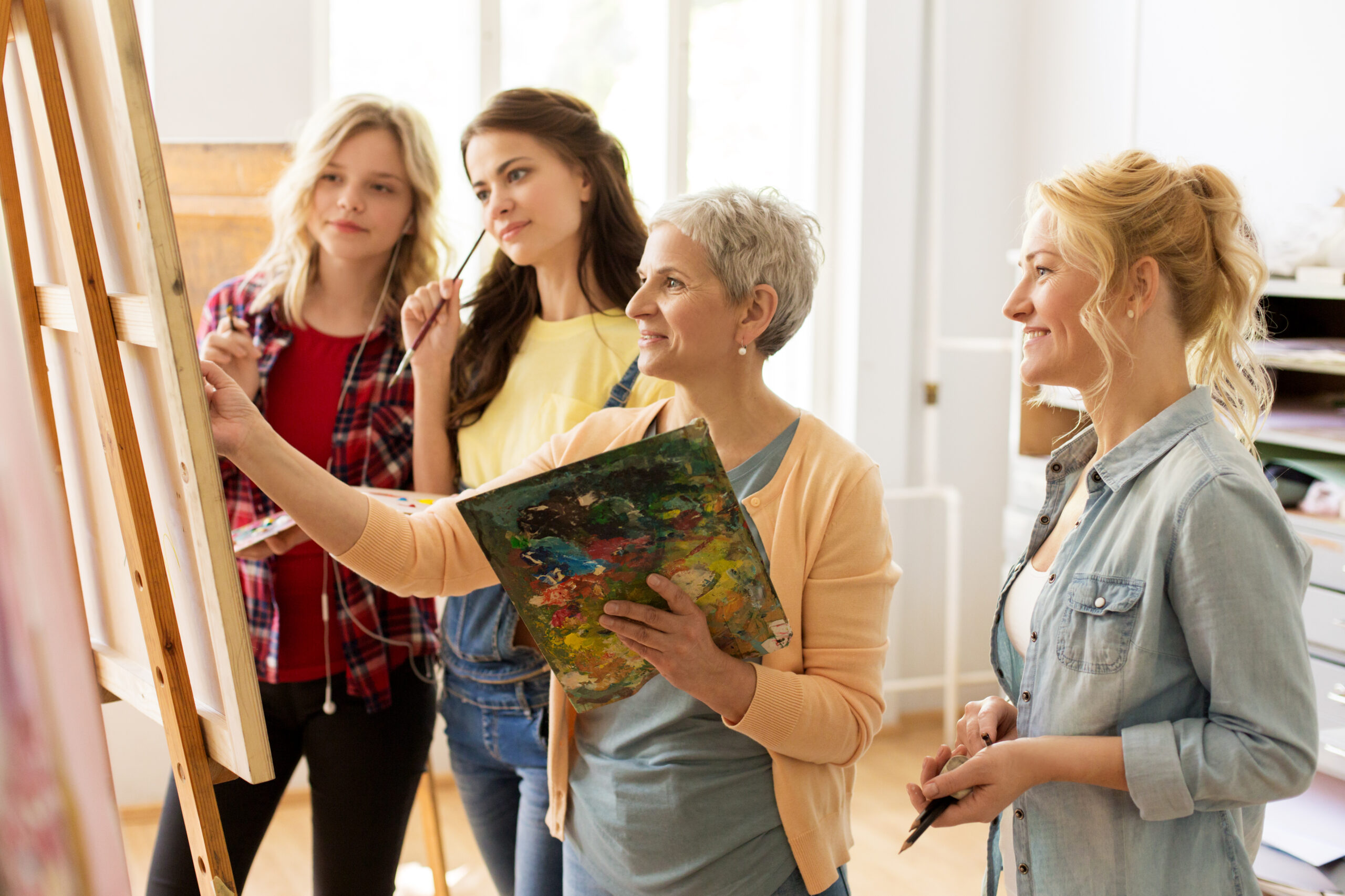 Stock photo of four women gathered around an easel painting.
