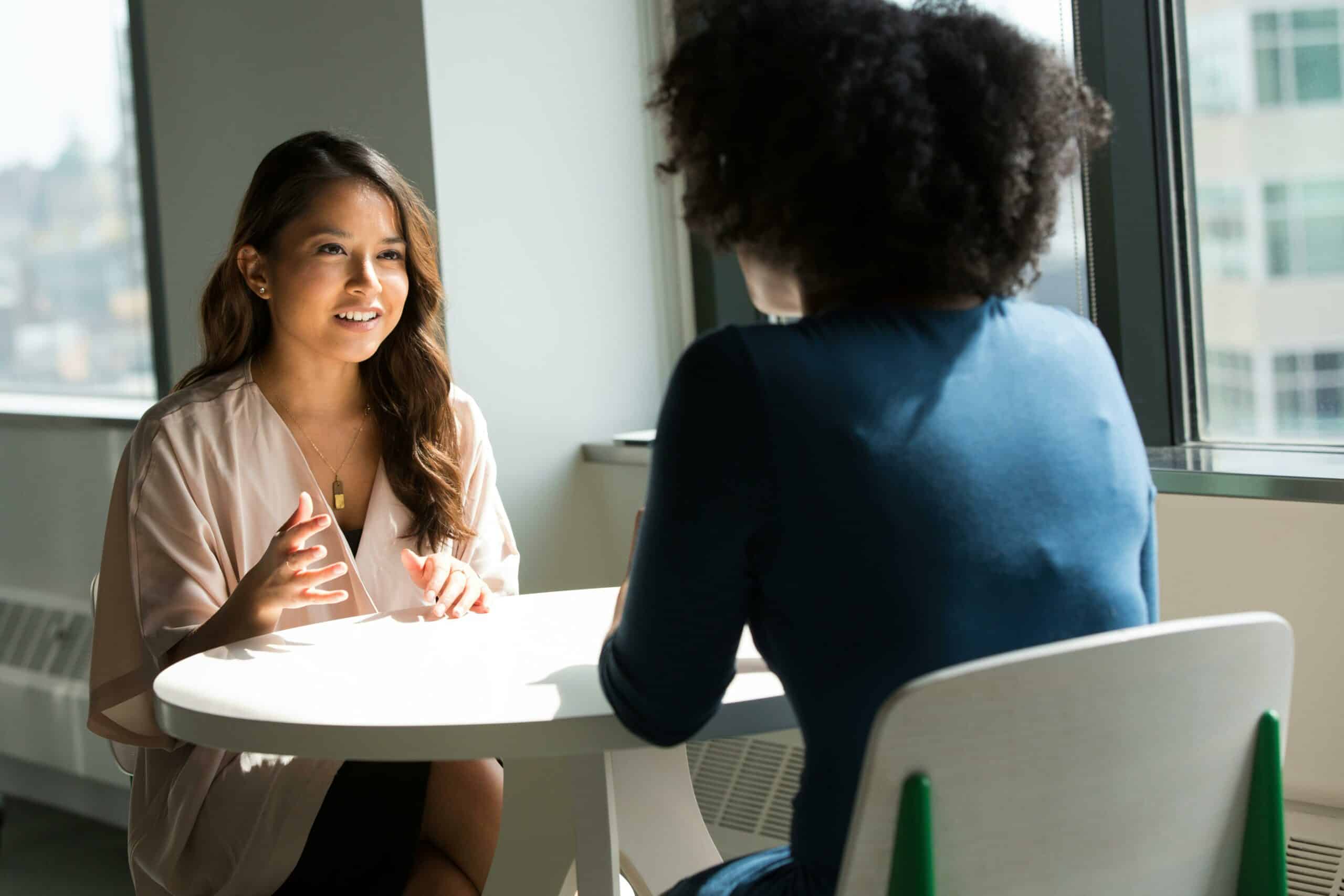 Stock photo of a young woman sitting across the table from another woman, deep in conversation.