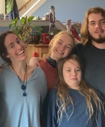 Photo of a woman with her brown hair pulled back, two girls ages 21 and 11, and an 18-year-old boy with shoulder-length brown hair and a beard. They are smiling at the camera except for the 11-year-old girl in the front, who's making a silly face.