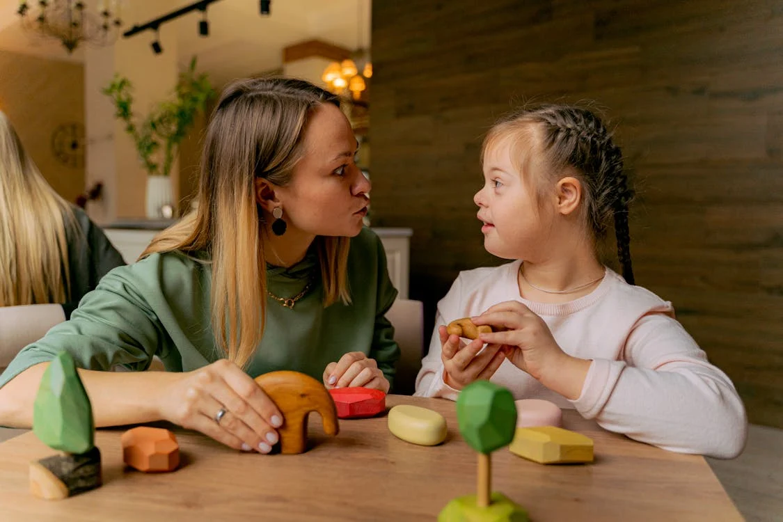 Stock photo of a woman playing with wooden toy blocks with a young girl with Down syndrome.
