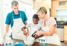 Helping Foster and Adopted Kids Feel Welcome for the Holidays Stock photo of a young Black boy mixing ingredients in a bowl as his white parents help him. They are wearing white aprons and are standing in the kitchen together.