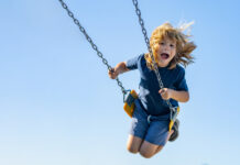 Stock photo of a young boy swinging high on a playground swing.