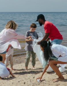 Stock photo of three adults and two kids picking up plastic trash on the shore of a beach.