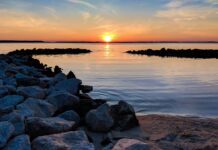 Stock photo of a sunrise over the ocean on a rocky, serene beach.