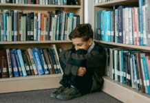 Mental Health in Middle Childhood Stock photo of a young boy crouched into a corner in a library.