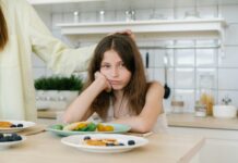 Turning Picky Into Adventurous Eaters Stock photo of a girl sitting at the dinner table with her head resting on her hand. She has a glum expression on her face and isn't touching the plate of food in front of her.
