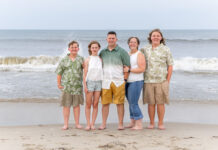 Photo of a family of five standing on the shore of a beach. There is a man, a woman, two boys and a girl.