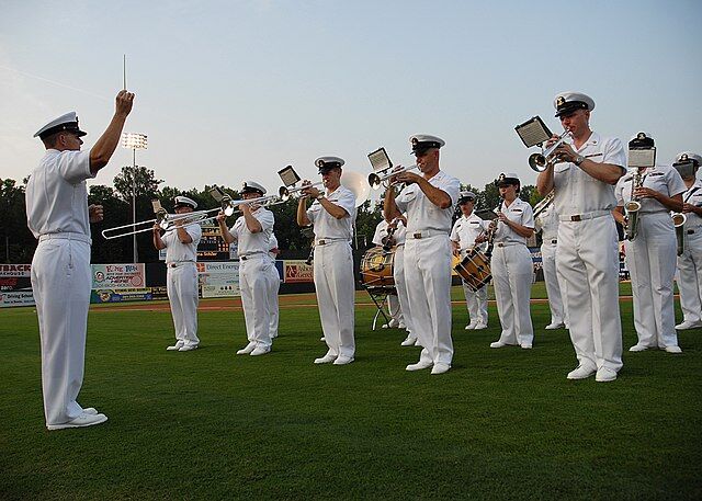 Photo of soldiers dressed in all-white uniforms playing instruments on a field.