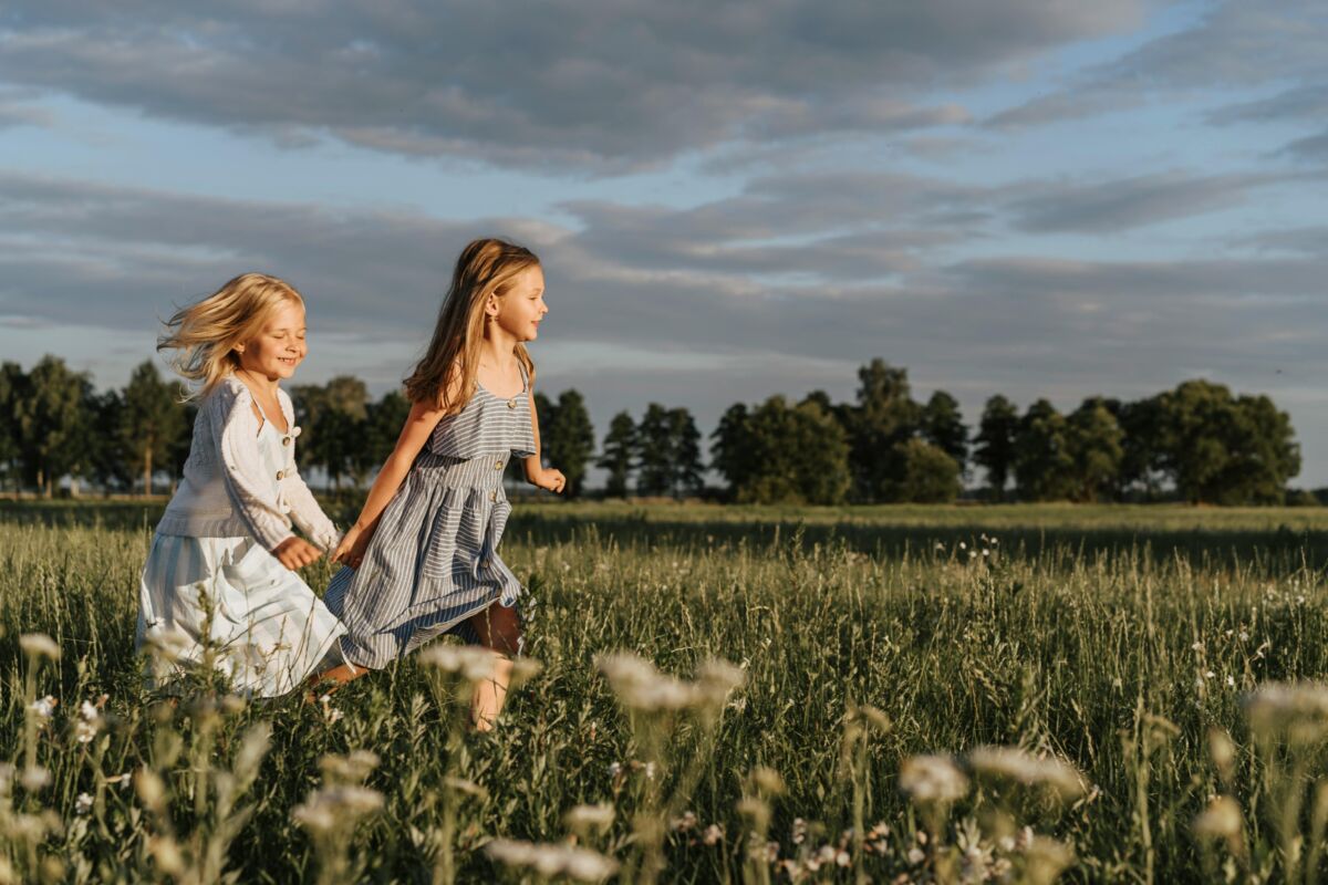 Stock photo of two young girls running through a field holding hands.