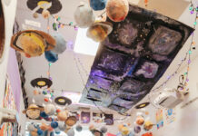 Photo of a classroom with three-dimensional planets hanging from the ceiling. Kids read on the carpet.