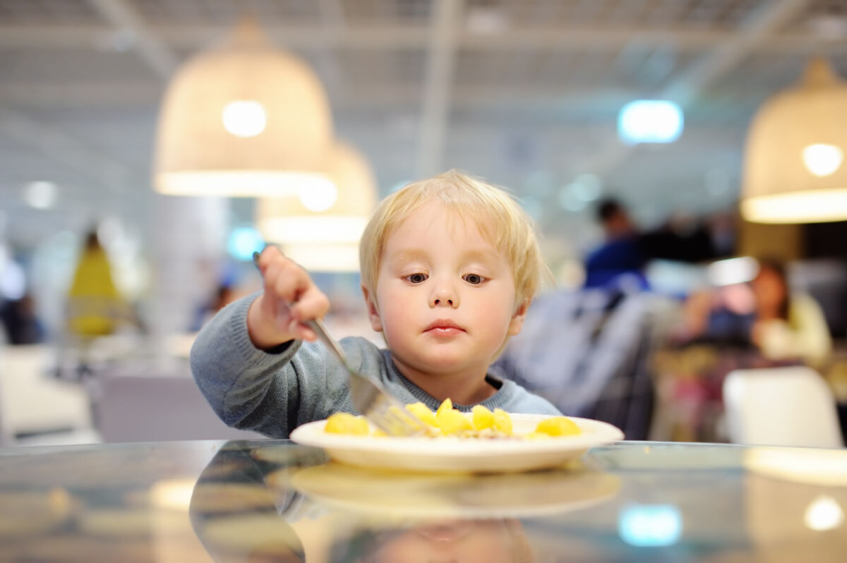 toddler boy eating potatoes in indoors cafe