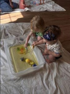 Two babies playing with a container of sand