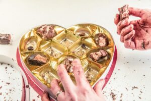 Two hands grabbing chocolates from a heart-shaped box