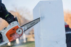 Person carving a block of ice with a chainsaw