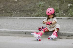 A girl in roller skates and safety gear sitting on a curb