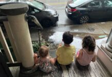 Three children sitting on a porch watching the rain