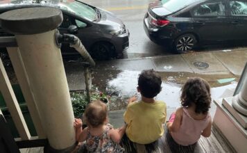 Three children sitting on a porch watching the rain