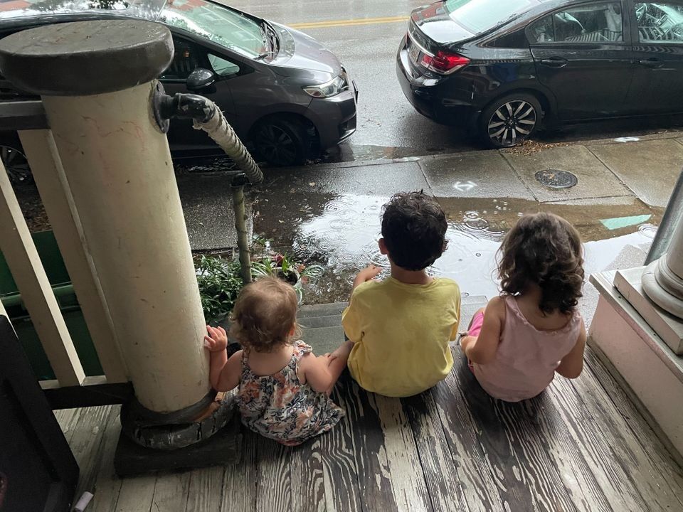 Three children sitting on a porch watching the rain