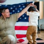 A woman and child interact playfully under an American flag indoors