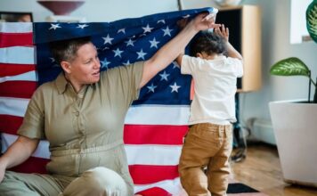 A woman and child interact playfully under an American flag indoors
