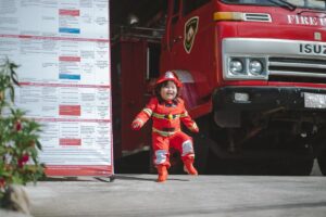A child dressed as a firefighter stands by a fire truck