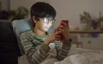 A boy wrapped in a blanket while using a smartphone
