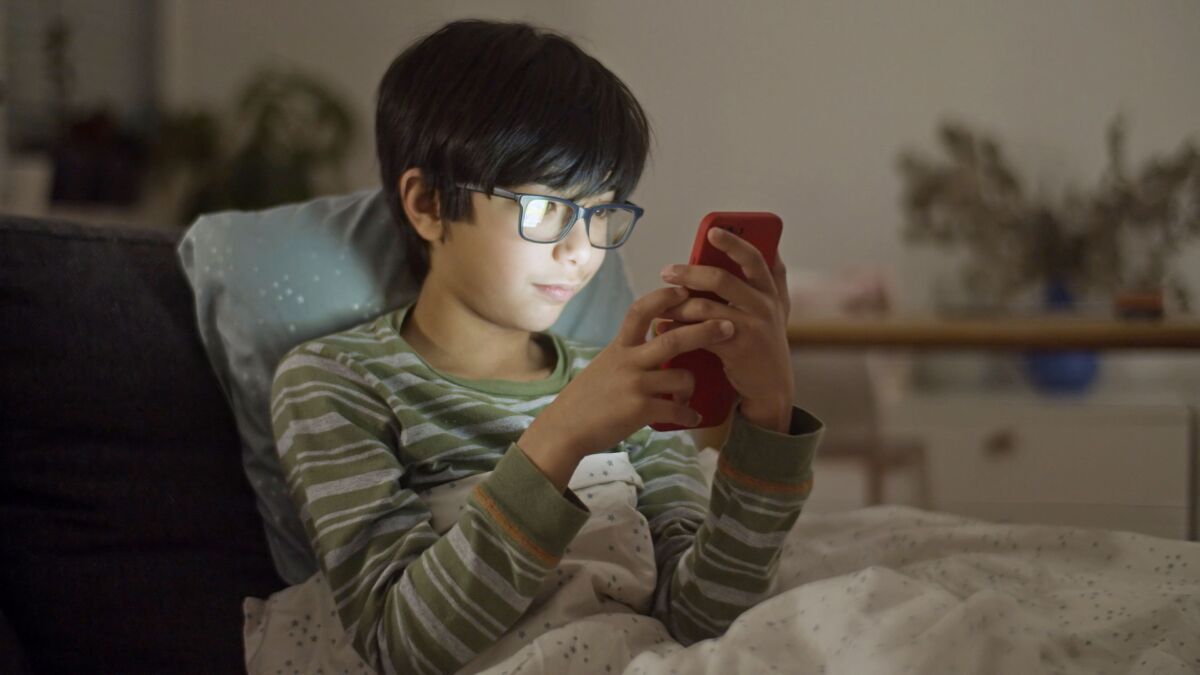 A boy wrapped in a blanket while using a smartphone