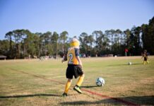 A school-age girl practices kicking a soccer ball on an athletic field.