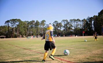 A school-age girl practices kicking a soccer ball on an athletic field.