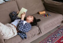A teenage girl lays on the couch looking at a notebook