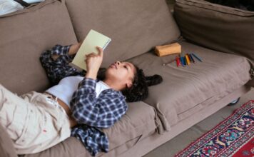 A teenage girl lays on the couch looking at a notebook