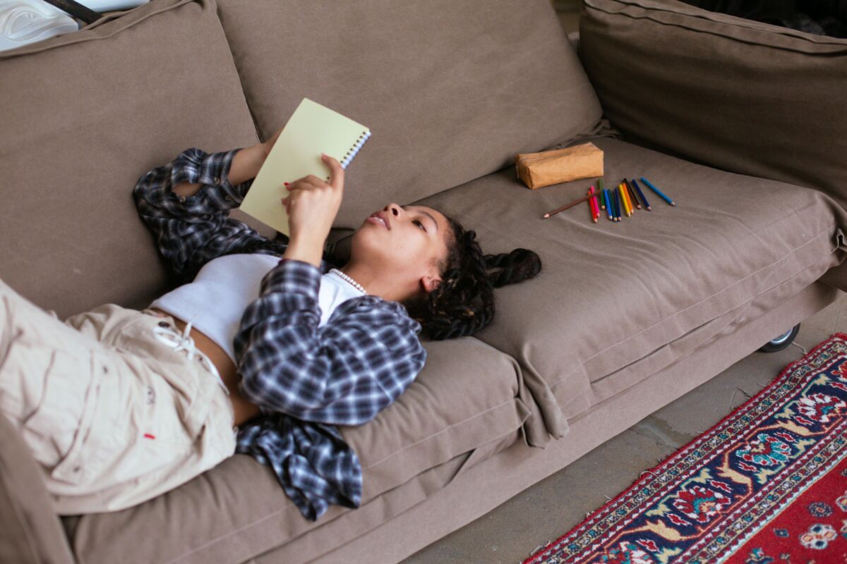 A teenage girl lays on the couch looking at a notebook