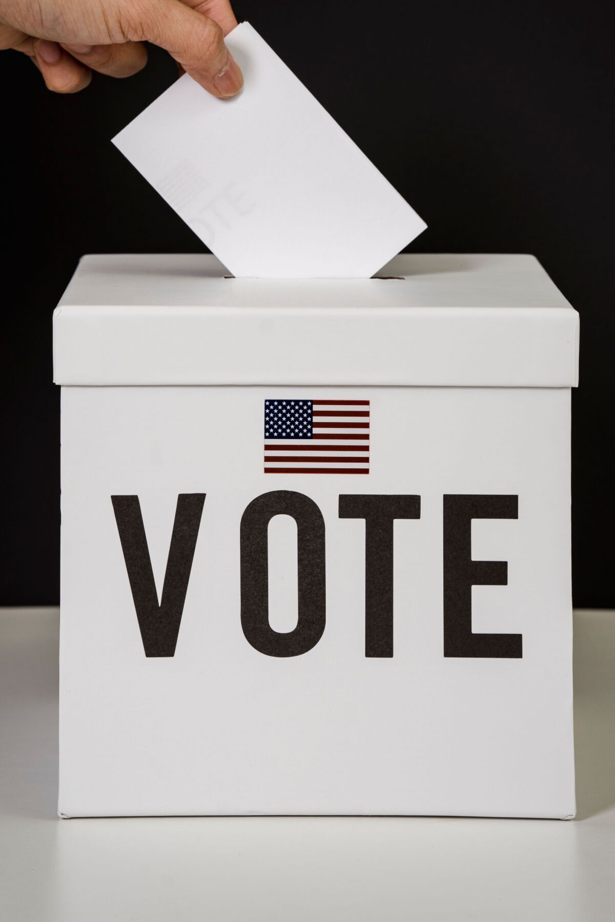 Person putting a ballot into a box that says "Vote"